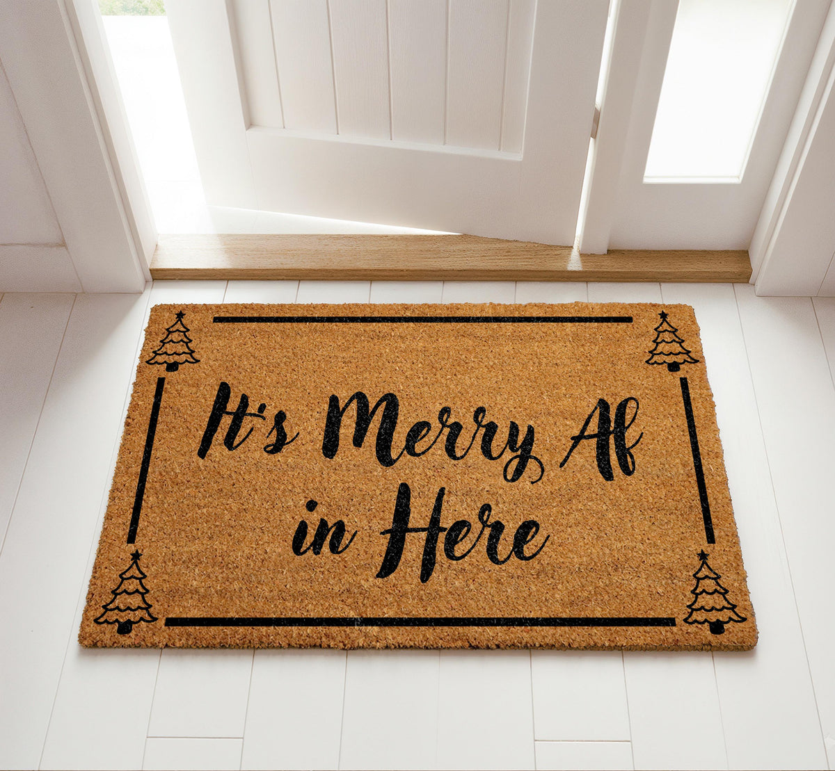 Doormat with "It’s merry AF in here" script lettering and a tree border
