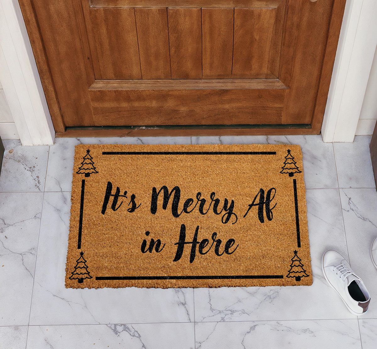 Doormat with "It’s merry AF in here" script lettering and a tree border